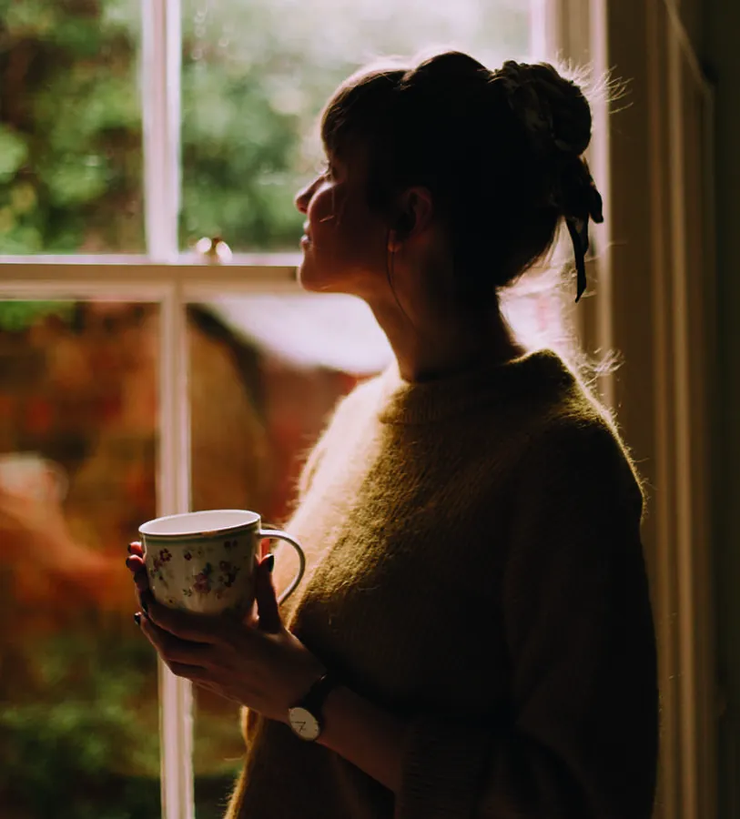 Mulher tomando café junto à janela